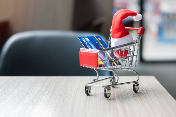 ミニチュアサンタの句の帽子、オフィスでテーブルの上のショッピングカートとクレジットカードでメリークリスマス。休日、お祝い、技術、電子商取引、ブラック・フライデー、サイバー・マンデー、オンライン決済の概念 - 写真・画像