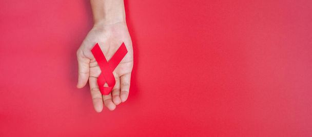 Hand holding Red Ribbon for supporting people living and illness. Healthcare and safe sex concept. December World Aids Day and multiple myeloma Cancer Awareness month - 写真・画像
