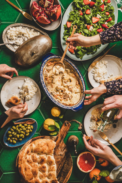 Family having Turkish dinner. Flat-lay of people hands over table with lamb in yogurt sauce, fresh arugula and strawberry salad, rice pilav and flatbread, top view. Ramazan iftar supper, celebration - Fotoğraf, Görsel