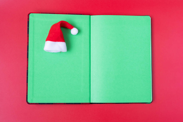 Buon Natale con Babbo Natale in miniatura con quaderno su sfondo rosso. Vacanza, Risoluzione, Capodanno, nuovo, e per fare concetto di lista - Foto, immagini