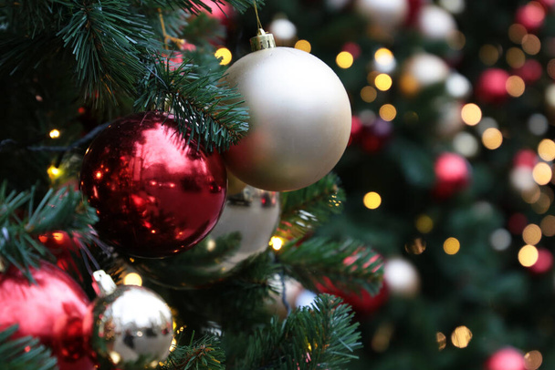 Christmas toys hanging on a fir branches on blurred festive lights background. New Year tree with decorations - 写真・画像