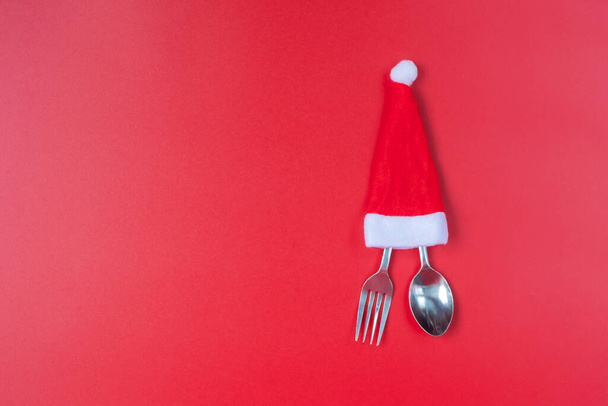 Feliz Navidad con Papá Noel en miniatura, tenedor y cuchara sobre fondo rojo. Navidad, fiesta y feliz Año Nuevo concepto - Foto, imagen