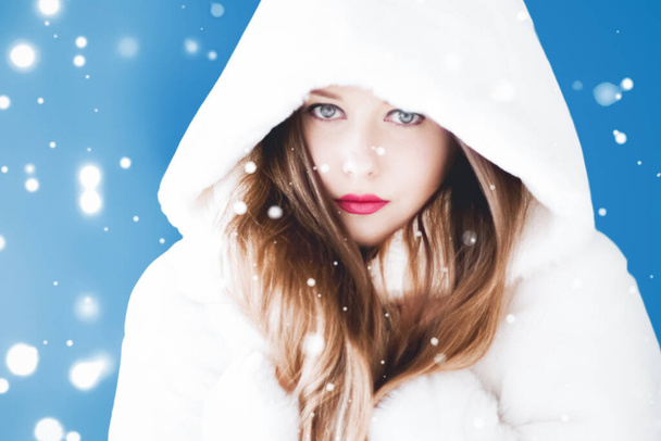 Frohe Weihnachten und Winterurlaub Porträt einer jungen Frau in weißem Kapuzenpelzmantel, Schnee auf blauem Hintergrund, Mode und Lifestyle - Foto, Bild