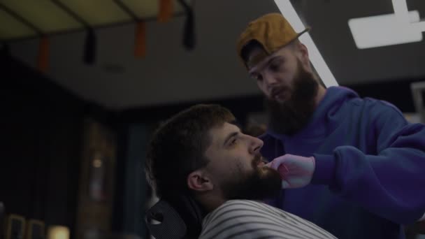 Un barbudo se corta la barba en una peluquería. Hombre peluquero peinando cabello y cortando con tijeras - Imágenes, Vídeo