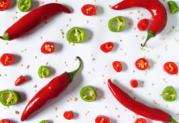 Vier rode hete paprika 's omgeven door gehakte rode en groene paprika' s op een wit oppervlak. - Foto, afbeelding