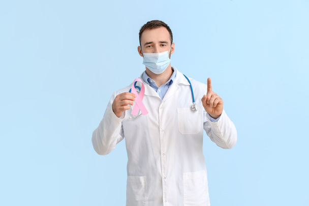 Tıbbi maskeli ve pembe kurdeleli bir doktor. Göğüs kanseri farkındalığı konsepti - Fotoğraf, Görsel
