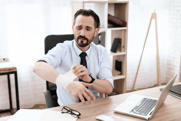 A man sits at work and rewinds an injured hand.  - Zdjęcie, obraz