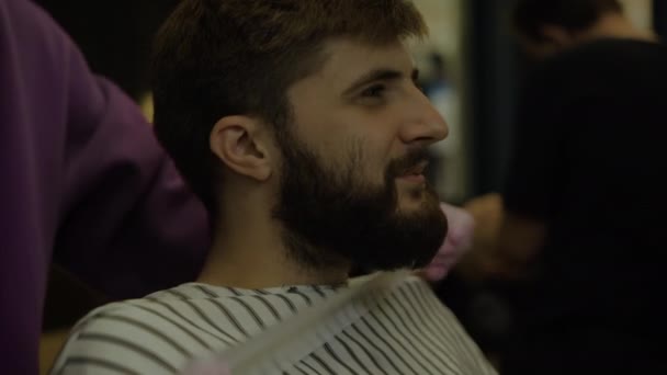 bearded man sitting in a barbershop. Fix the cape for the client - Footage, Video