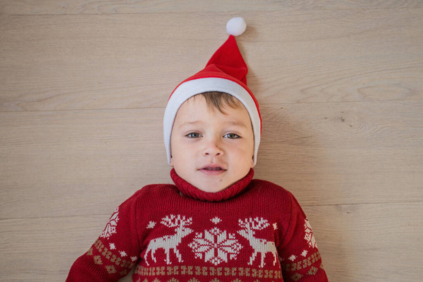 Poika joulun villapaita ja santa hattu makaa puulattialla - Valokuva, kuva