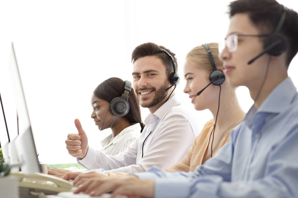Feliz operador de centro de llamadas masculino mostrando gesto de pulgar hacia arriba, trabajando con sus colegas en la oficina moderna - Foto, Imagen