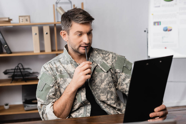 στρατιώτης με στρατιωτική στολή κρατώντας στυλό και κοιτάζοντας το πρόχειρο  - Φωτογραφία, εικόνα