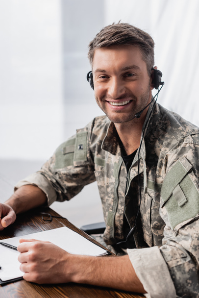 militaire positif en uniforme et casque souriant au bureau - Photo, image
