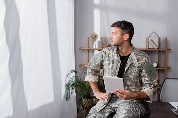 voják ve vojenské uniformě držící digitální tablet a odvracející se v úřadu - Fotografie, Obrázek