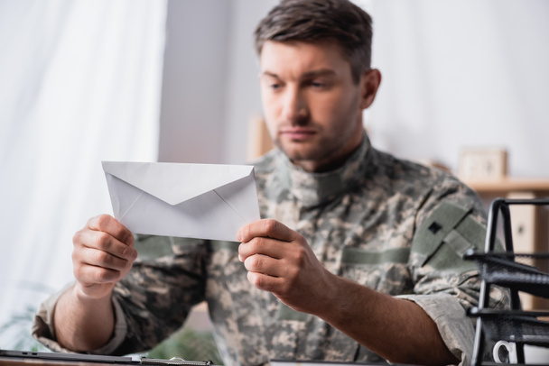 weißer Umschlag in den Händen eines Soldaten auf verschwommenem Hintergrund - Foto, Bild