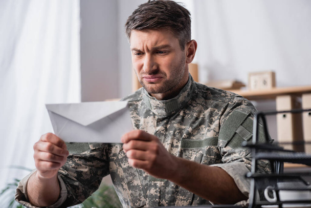 white envelope in hands of displeased soldier on blurred background - Zdjęcie, obraz