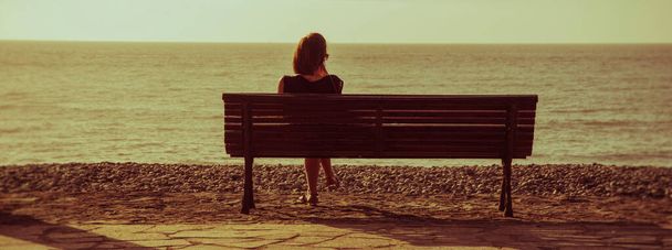 Sylwetka młodej kobiety siedzącej samotnie na ławce przed oceanem - Zdjęcie, obraz