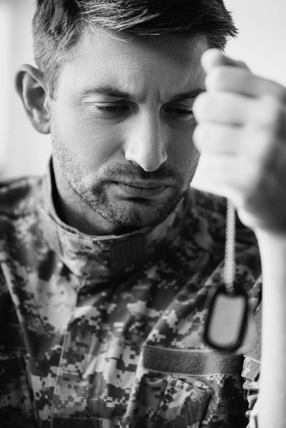 λυπημένος στρατιώτης με στολή καμουφλάζ κρατώντας στρατιωτική ετικέτα, μονόχρωμη - Φωτογραφία, εικόνα