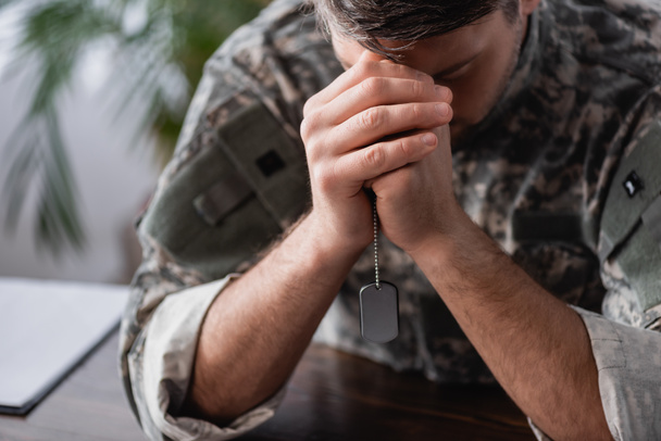 soldado triste em uniforme de camuflagem segurando tag militar em mãos apertadas - Foto, Imagem