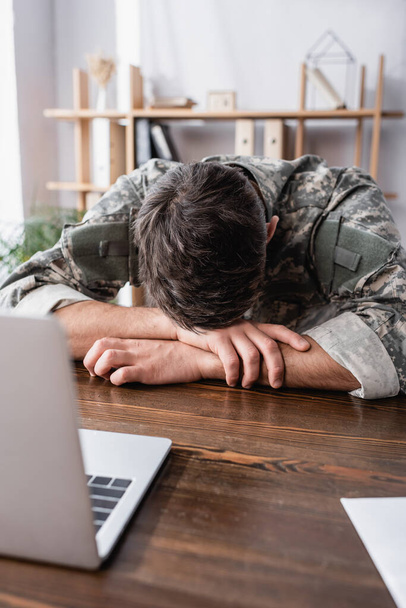 Soldat in Uniform liegt auf Schreibtisch neben Laptop - Foto, Bild
