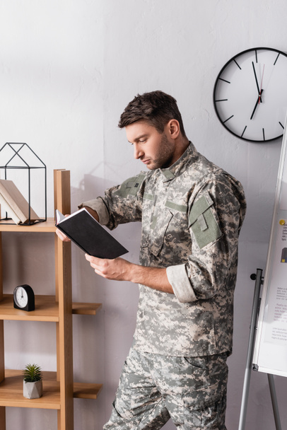 serious military man holding notepad near wooden rack - Photo, Image