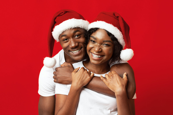 Young black lovers in Santa hats having fun on red - Φωτογραφία, εικόνα