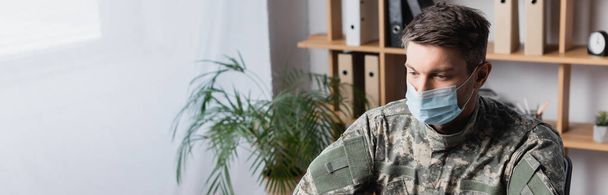 vojenský muž v uniformě a lékařské masce dívá pryč, prapor - Fotografie, Obrázek