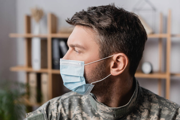 Katonai férfi egyenruhában és orvosi maszkban, félrenéz. - Fotó, kép