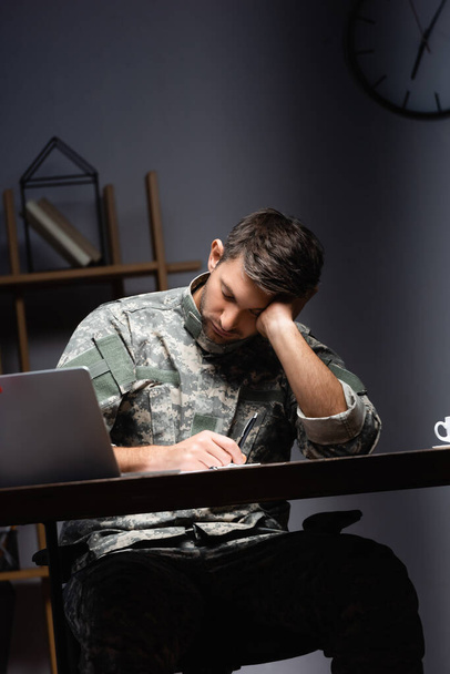 уставший военный в форме спит рядом с ноутбуком в офисе - Фото, изображение