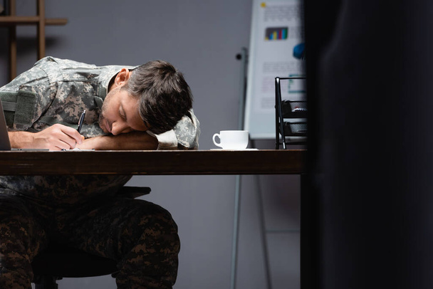 tired military man in uniform sleeping near cup in office - Foto, imagen