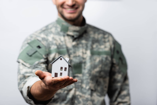 modèle de maison en main de l'homme militaire heureux en uniforme sur fond flou isolé sur blanc - Photo, image