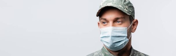 militar en uniforme y máscara médica mirando hacia otro lado aislado en blanco, bandera - Foto, Imagen