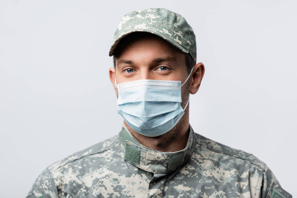 uomo militare in uniforme e maschera medica guardando la fotocamera isolata su bianco - Foto, immagini