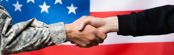 vista recortada del soldado estrechando la mano con el hombre civil cerca de la bandera americana sobre fondo borroso, bandera - Foto, Imagen