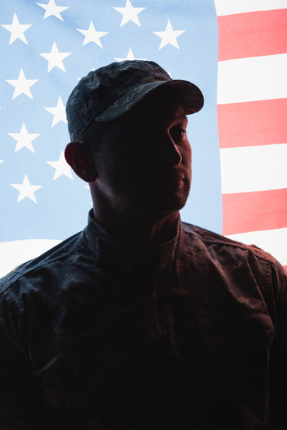 制服を着た愛国的な軍人とアメリカ国旗の近くの帽子を背景に - 写真・画像