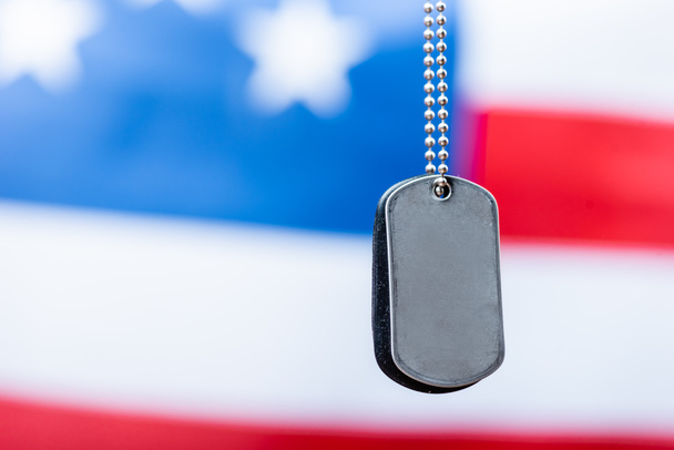 zblízka prázdný kovový odznak na řetězu poblíž americké vlajky na rozmazaném pozadí - Fotografie, Obrázek
