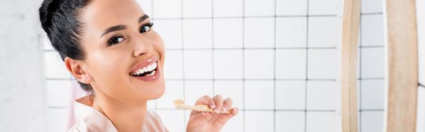 Allegro bruna donna che tiene lo spazzolino vicino allo specchio in bagno, banner  - Foto, immagini