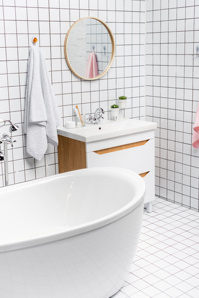 White bathtub near towel and sink in modern bathroom  - Foto, imagen