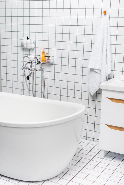 Toiletries near towel and bathtub in modern white bathroom  - Фото, изображение