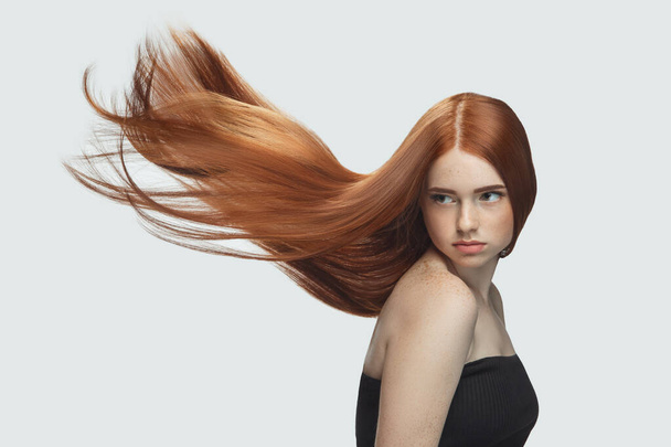 Beautiful model with long smooth, flying red hair isolated on white studio background. - Фото, зображення