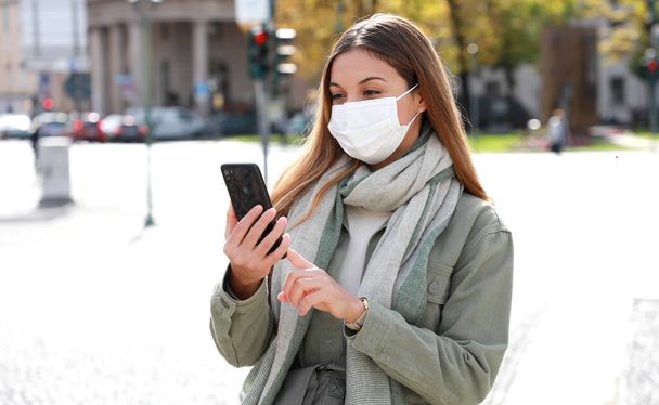 COVID-19 Mobile Application Νεαρή γυναίκα με χειρουργική μάσκα χρησιμοποιώντας Smart Phone App στην οδό City - Φωτογραφία, εικόνα