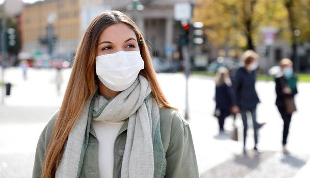 COVID-19 Социальная дистанцирующаяся женщина на городской улице в хирургической маске против вируса атипичной пневмонии SARS-CoV-2. Девушка в маске уважает социальное дистанцирование во время пандемии коронавируса 2019 года. - Фото, изображение