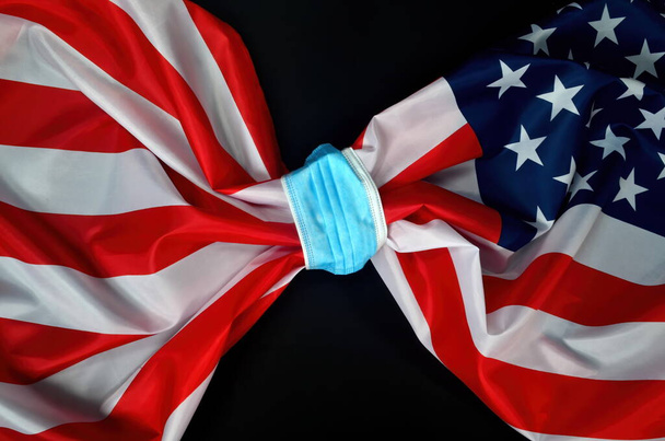 Flag of USA tied with a face protection mask. COVID - 19 problems in United States and in the world. Medicine, healthcare and virus concept. black background - Photo, Image