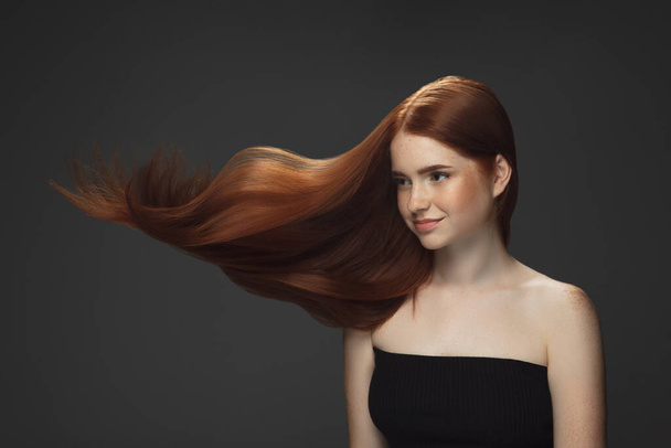 Beautiful model with long smooth, flying red hair isolated on dark studio background. - Foto, imagen