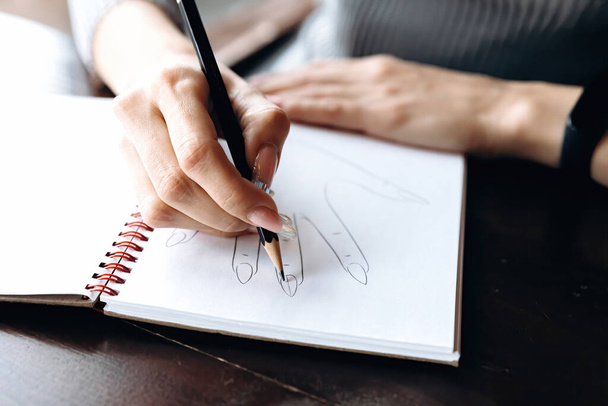 La manicurista hace un boceto del diseño de uñas en un cuaderno especial. - Foto, Imagen