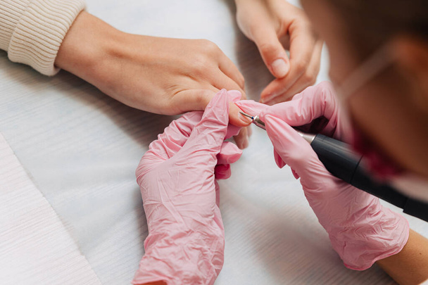 Manicure process. A master in pink rubber gloves polishes nails with an electric nail file. Female hands close up. - Fotoğraf, Görsel