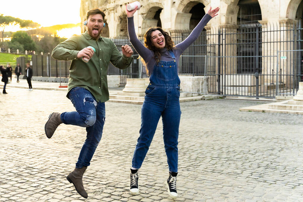 Молода пара туристів робить фотографії, які стрибають біля Колізею з таймером камери в романі. Романтична молода пара туристів слухає музику і п'є смачну коктейль
. - Фото, зображення