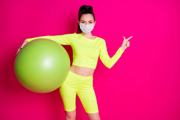 Positive sportswoman point finger copyspace stay home news wear medical mask isolated pink bright color background - Foto, imagen
