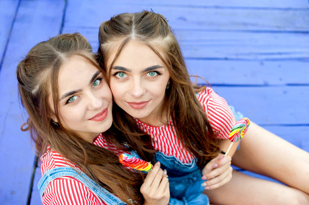 Beautiful teenage twin sisters in colorful clothes with lollipops sitting on colored boards, top view - Foto, Bild