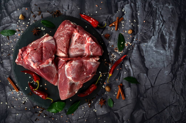 Νωπό ωμό κρέας προβάτου, απομονωμένο σε μαύρο πέτρινο φόντο με μπαχαρικά. Μεγάλο κομμάτι φιλέτου κρέατος ή φιλέτου closeup - Φωτογραφία, εικόνα