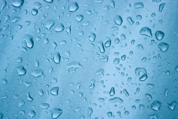 Σταγόνες βροχής στην ασημί-μπλε επιφάνεια του αυτοκινήτου. Επιλεκτική εστίαση. - Φωτογραφία, εικόνα